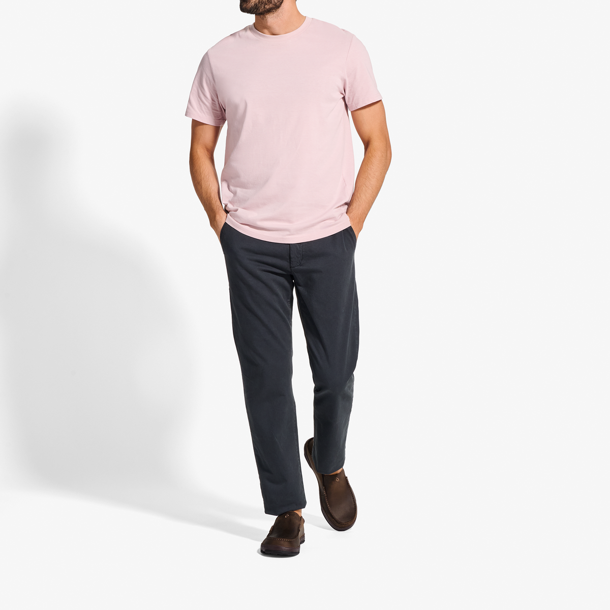 Man wearing light pink crew neck t-shirt, dark navy pants, and dark brown slip-on shoes.