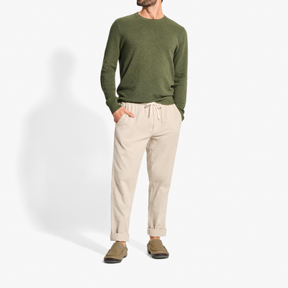 Man wearing olive green crewneck sweatshirt, cream pants, and tan suede slippers with dark soles.
