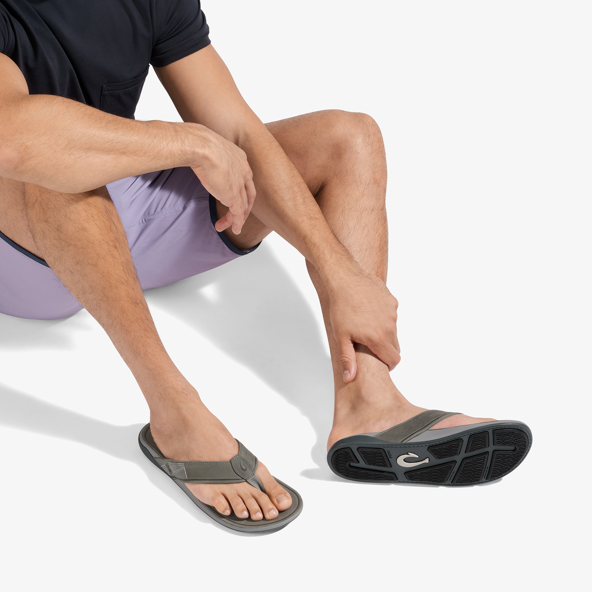Man wearing stone-colored thong sandals with black sole, paired with navy shirt and lavender shorts.