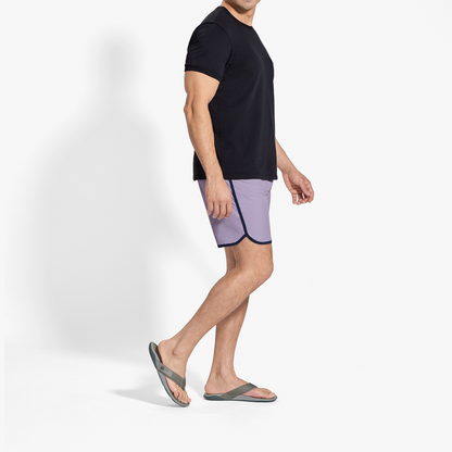 Man wearing black short-sleeve t-shirt and lavender shorts with dark trim, standing in profile view.