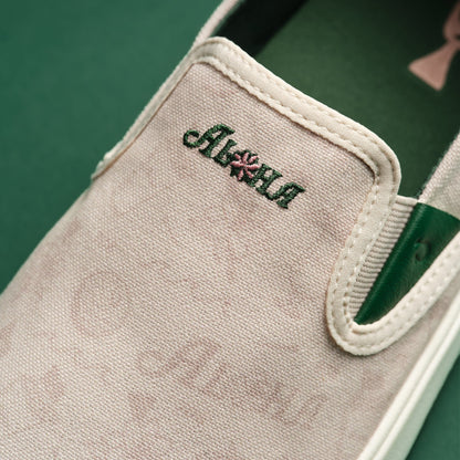 Cream canvas slip-on shoe with green stripe and embroidered brand text on the side.