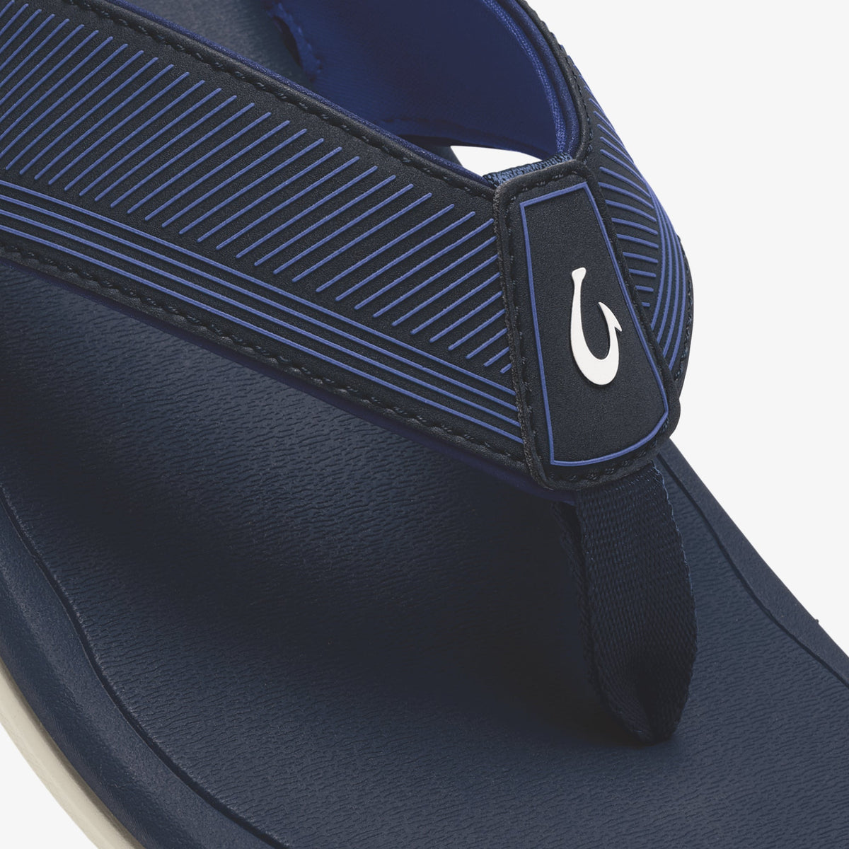 Navy blue flip-flop with horizontal striped upper strap, white hook logo, and cream-colored sole.