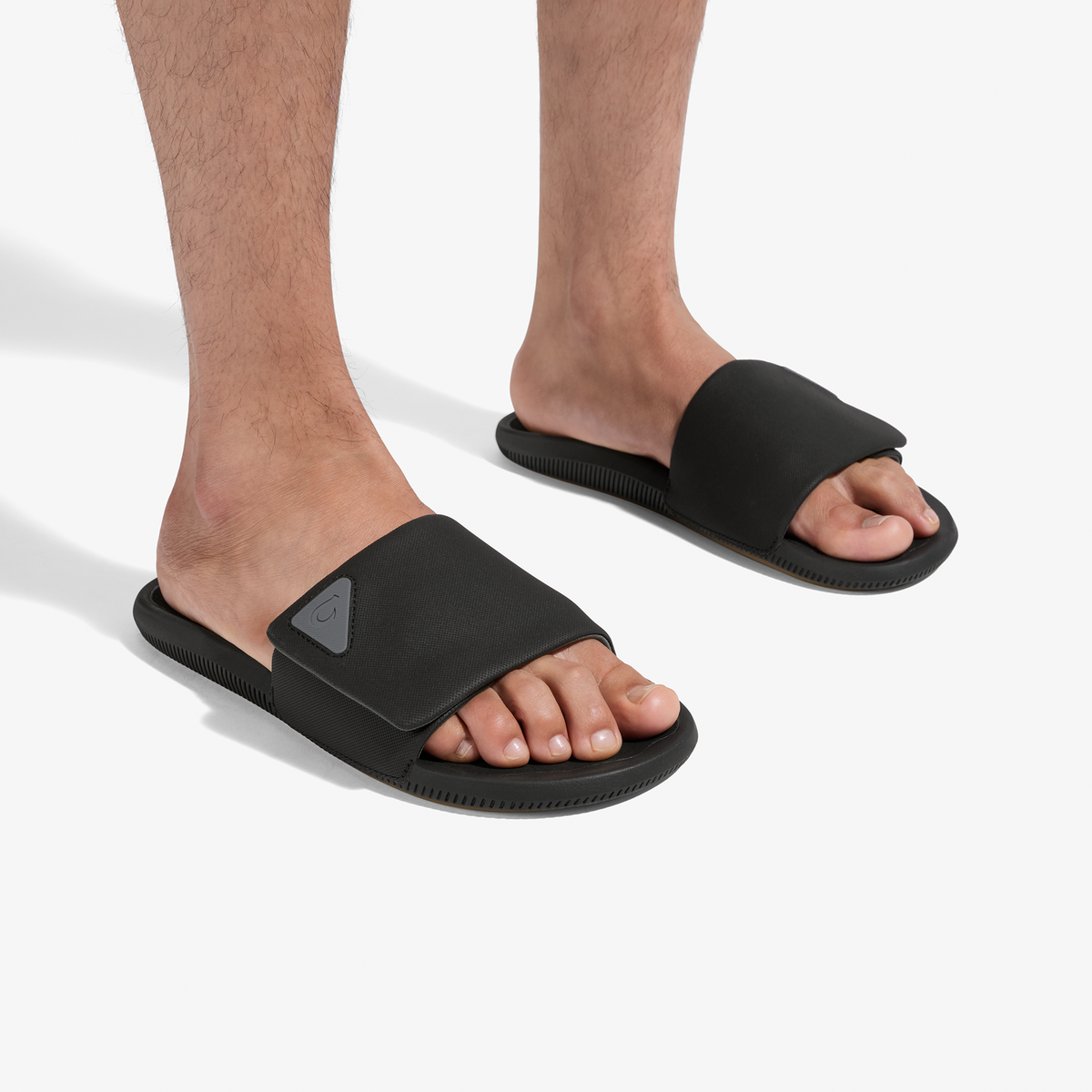 Man wearing black slide sandals with textured soles and triangle logo on upper.
