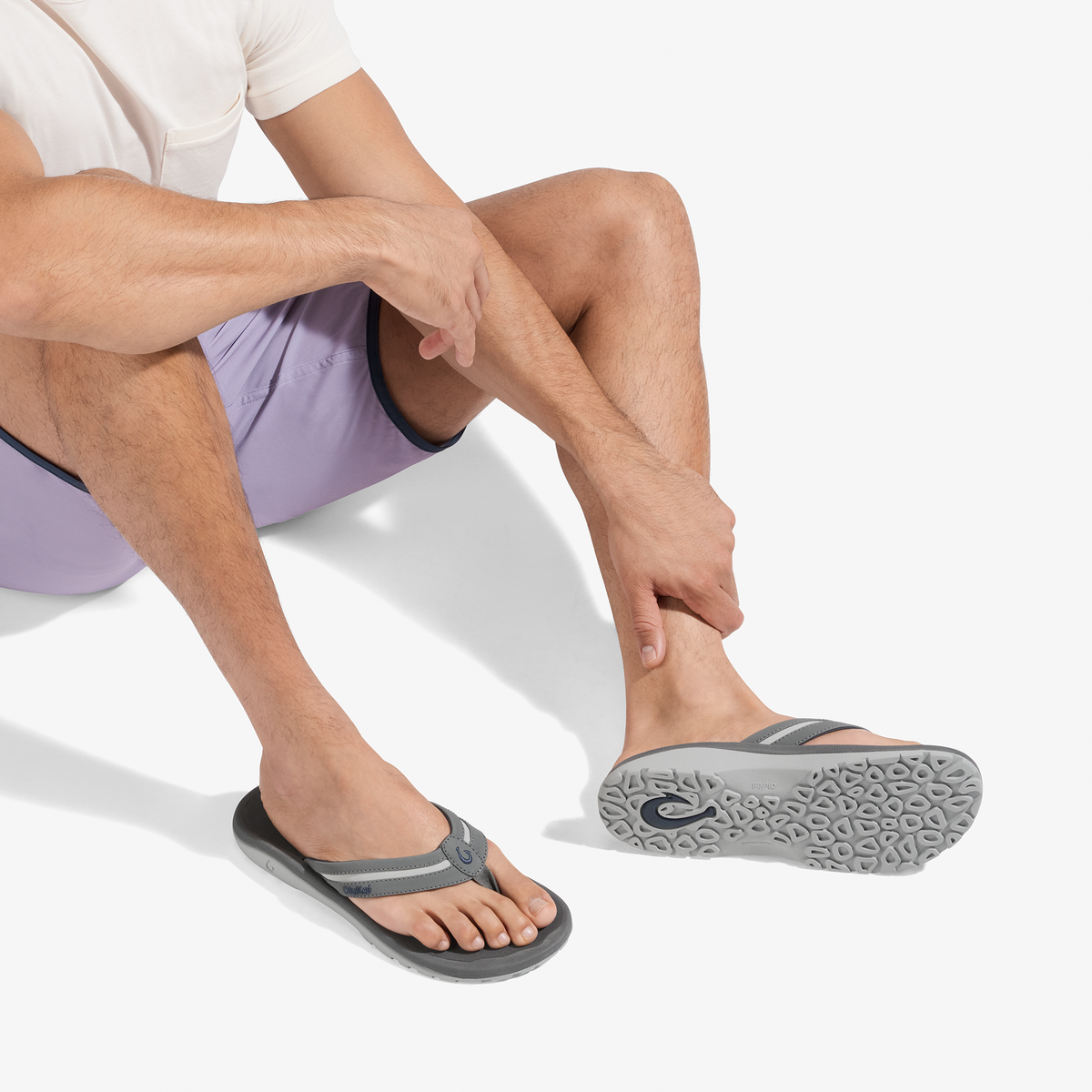 Man wearing grey and rock flip-flop sandal with textured sole, shown with purple shorts and white shirt.