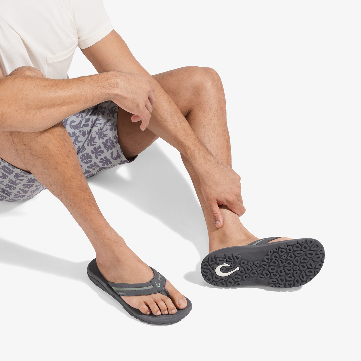 Man wearing grey and seagreen patterned shorts and dark grey thong sandals with textured sole.