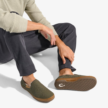 Olive green slip-on slipper with tan suede trim and textured sole, worn with dark jeans and cream sweater.