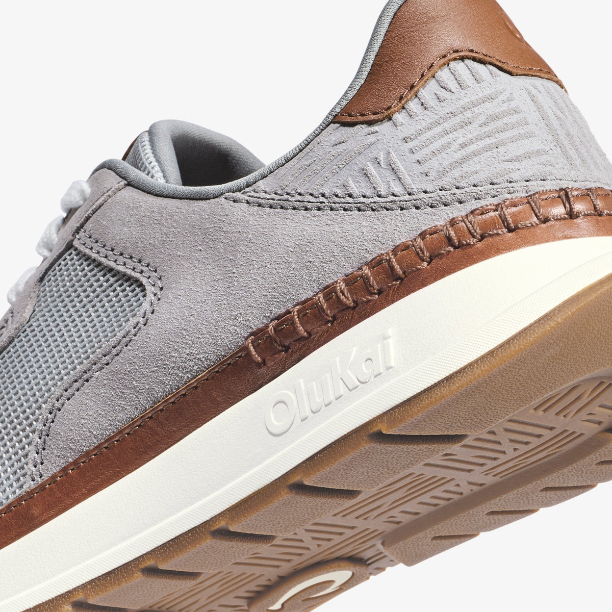 Light grey sneaker with brown leather heel tab, white midsole, and textured sole detail visible from side angle.