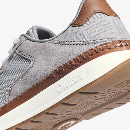 Light grey sneaker with brown leather heel tab, white midsole, and textured sole detail visible from side angle.