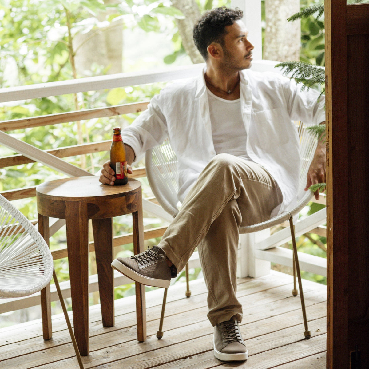 Small round walnut side table with tapered legs, styled on an outdoor deck with a person seated nearby holding a bottle.