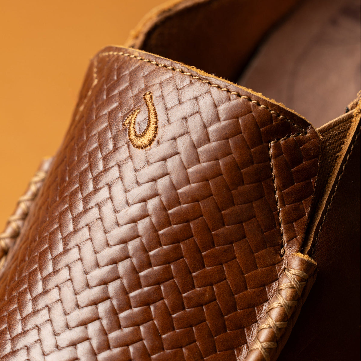 Toffee-colored woven lauhala bag with gold embroidered hook detail on front panel and dark java lining visible inside.