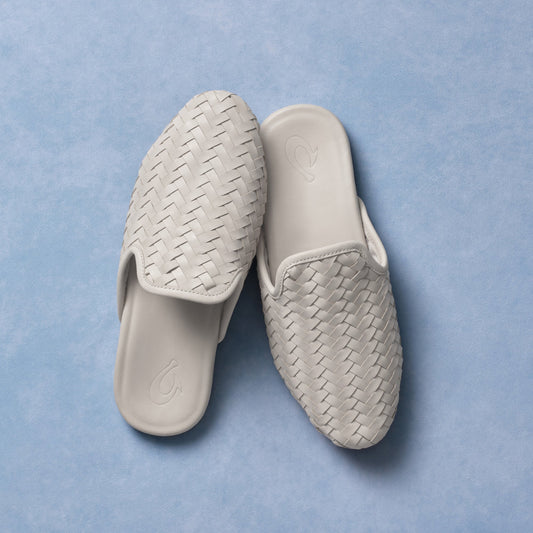 Pair of cream-colored slide sandals with woven textile uppers and smooth rubber soles displayed on blue background.
