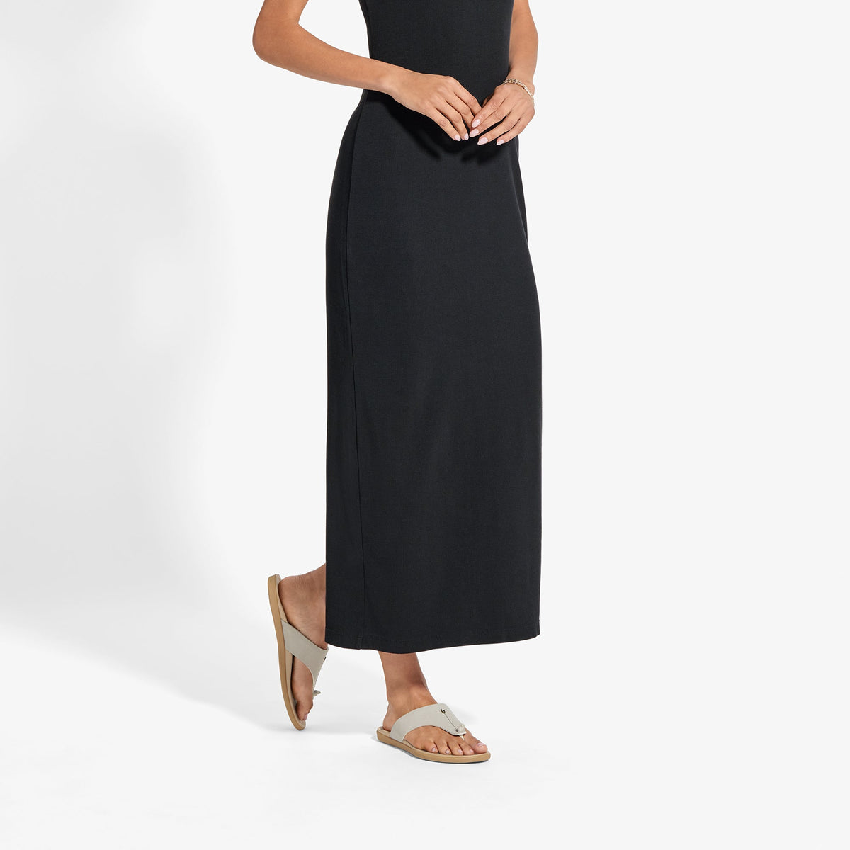 Person wearing black sleeveless maxi dress with tan slide sandals against white background.