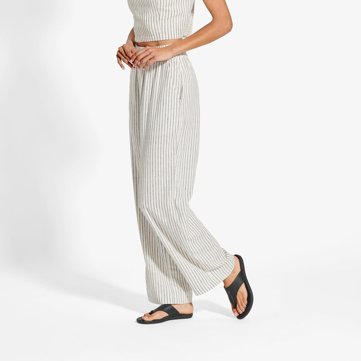 Woman wearing cream ribbed sleeveless top and matching wide-leg pants with black slide sandals.
