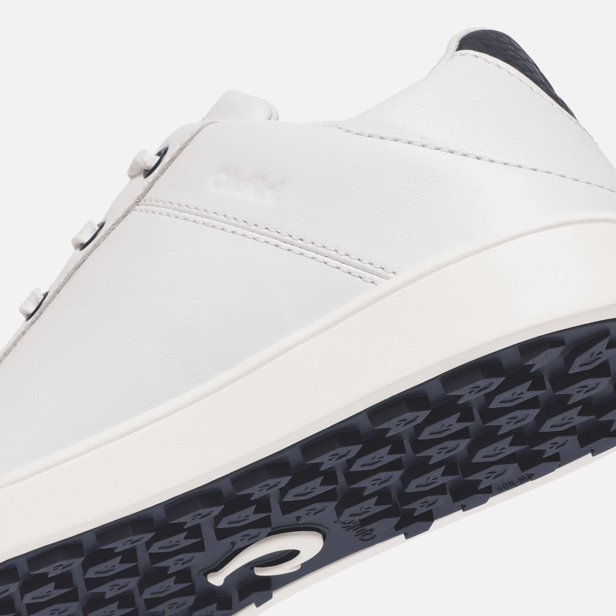 White leather sneaker with dark blue heel panel and patterned dark blue sole, featuring side stitching detail.