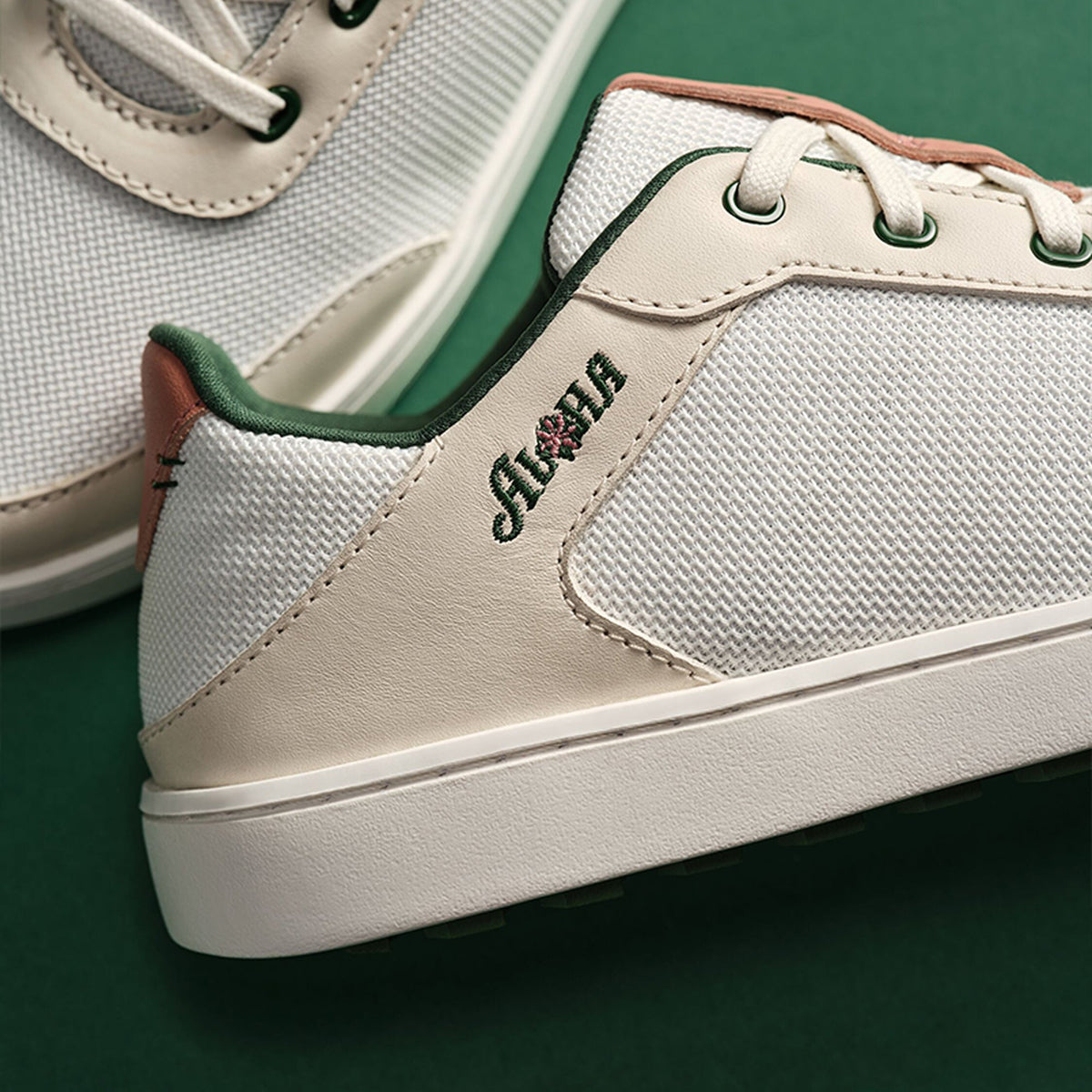 White canvas and leather sneaker with green heel trim and white sole, shown from side angle.