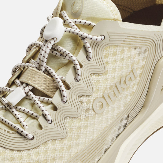 White and tan sneaker with striped laces, textured upper, and wavy sole detail with brand name.